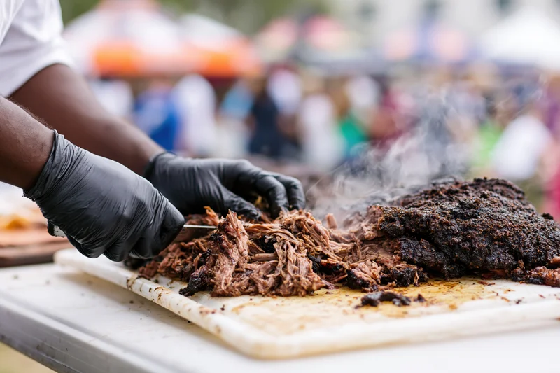 Pitmaster slicing smoked brisket on a white cutting board at an outdoor food festival