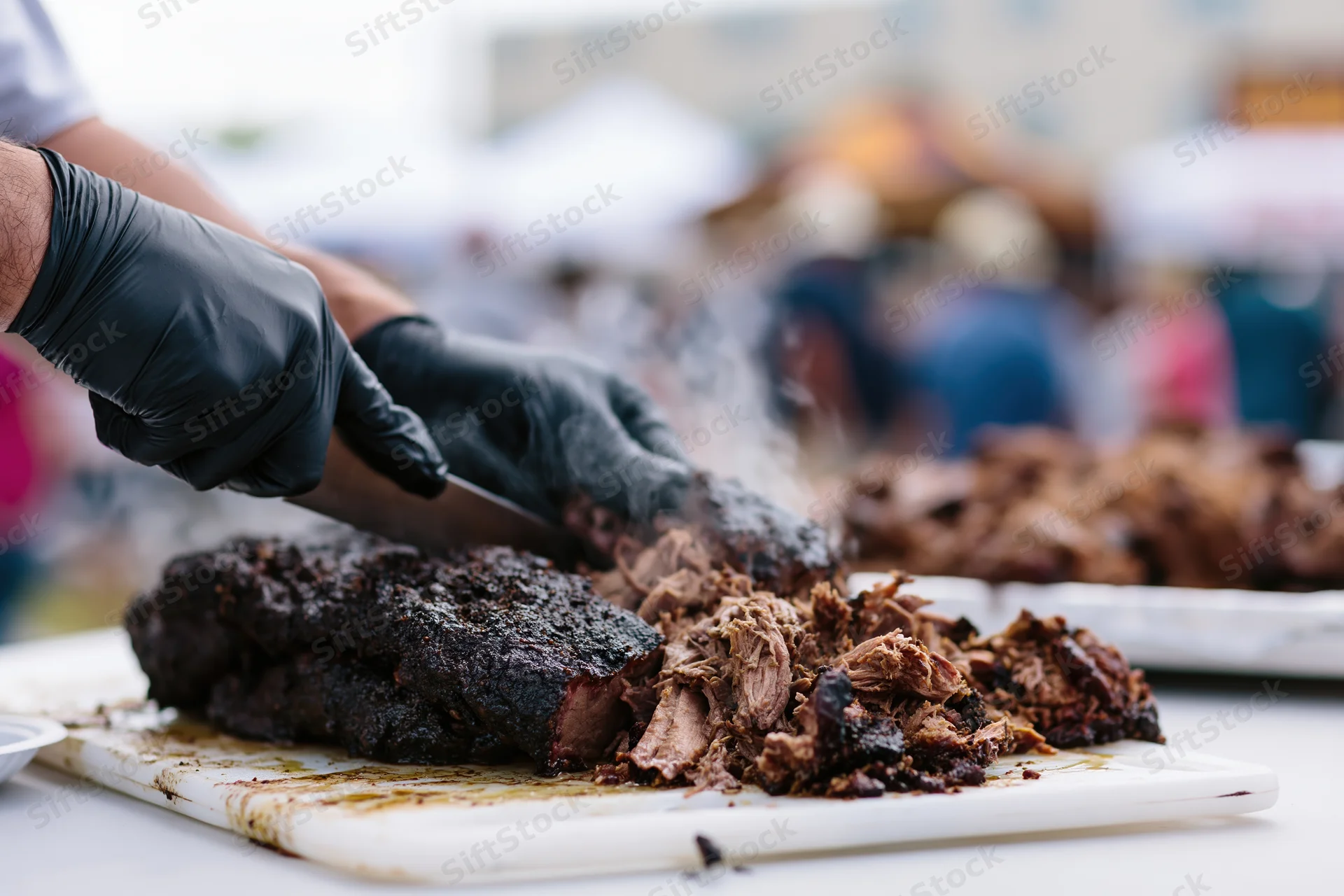 Pitmaster slicing and pulling smoked pork brisket on a cutting board at an outdoor food festival