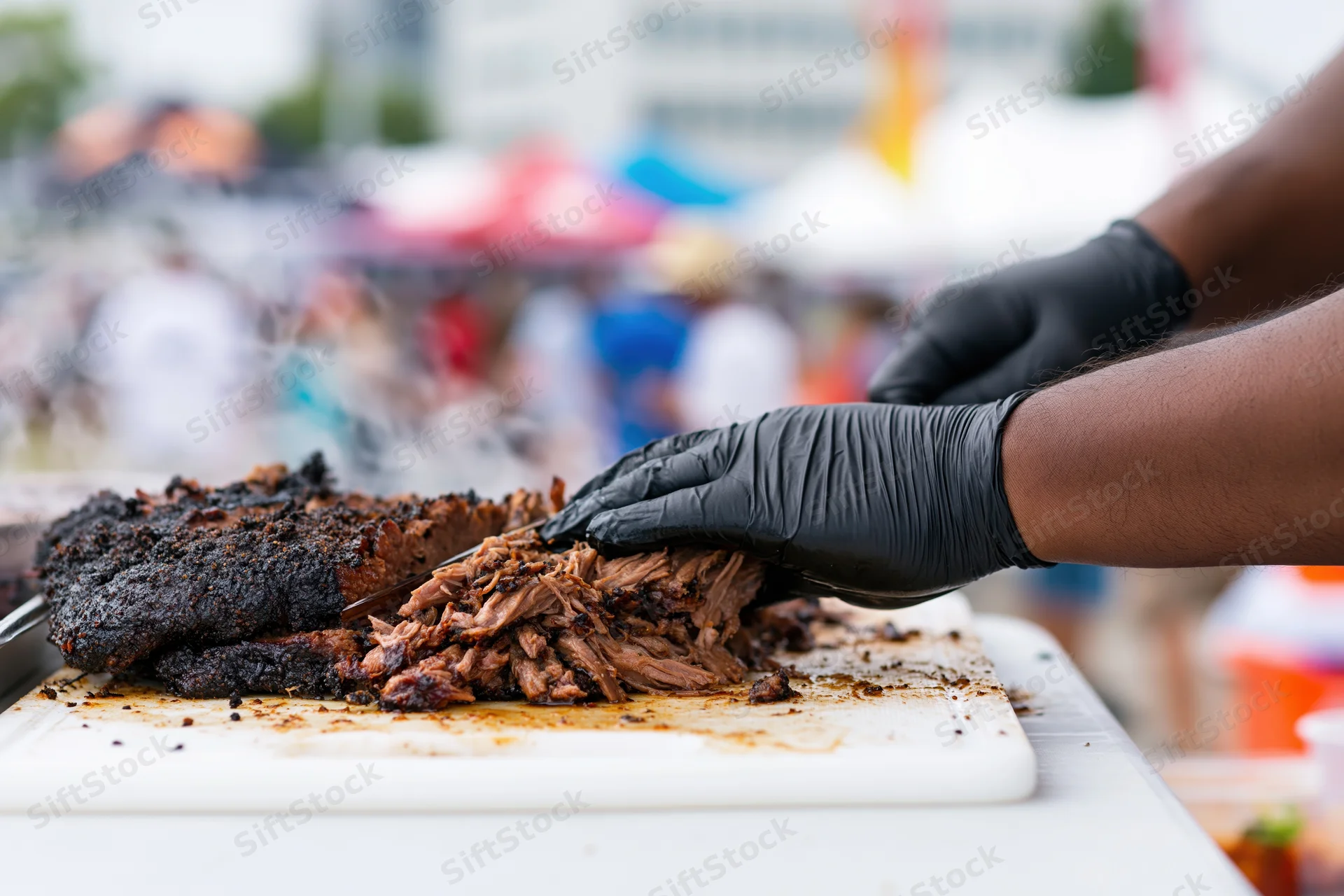 Pitmaster slicing and pulling smoked pork brisket on a white cutting board at an outdoor food festival