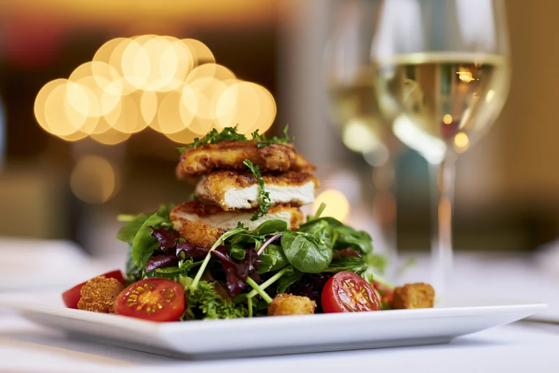 Plated salad with crispy chicken and mixed greens served with white wine on a restaurant table