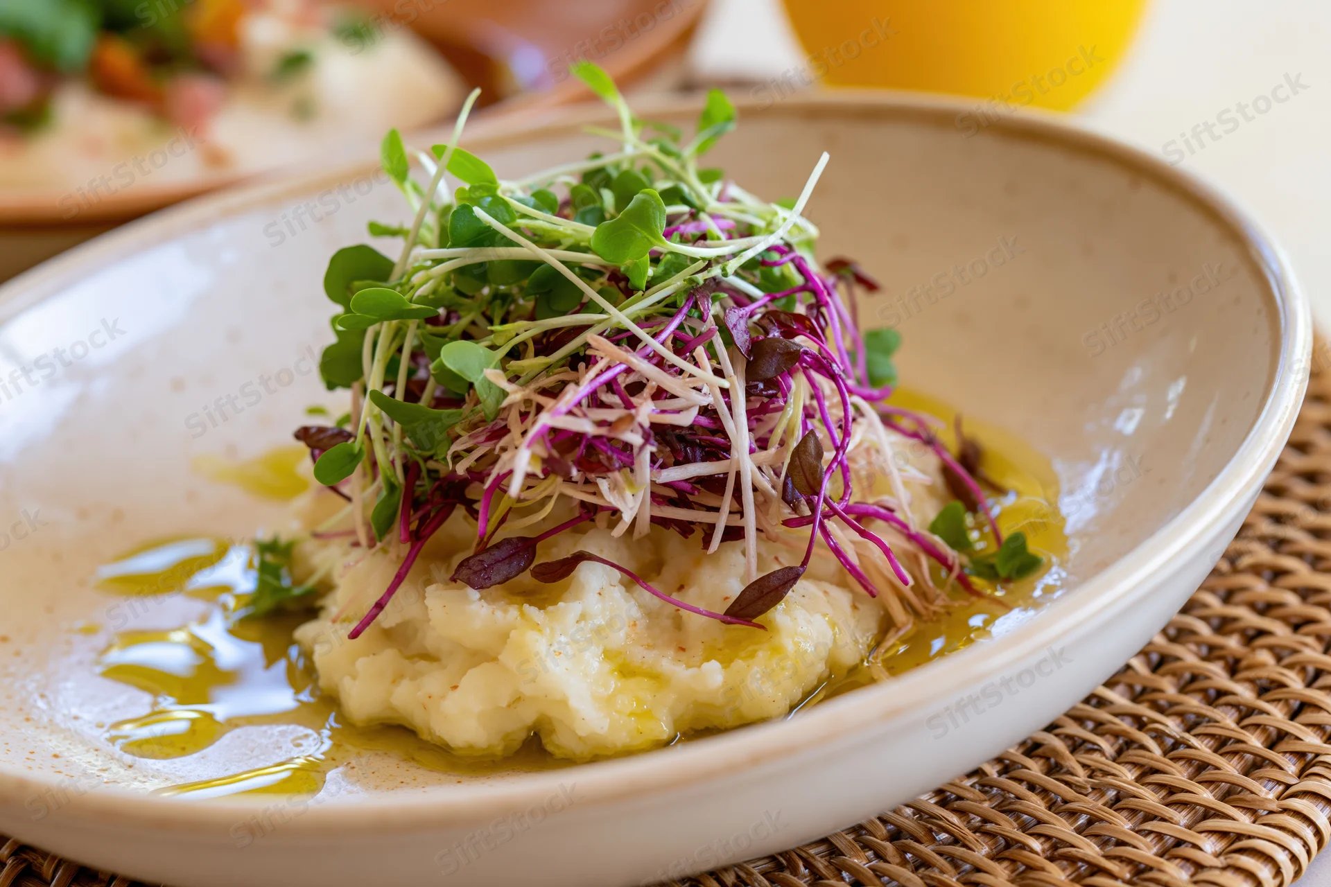 Mashed potato topped with colorful microgreens in a ceramic bowl on a woven placemat