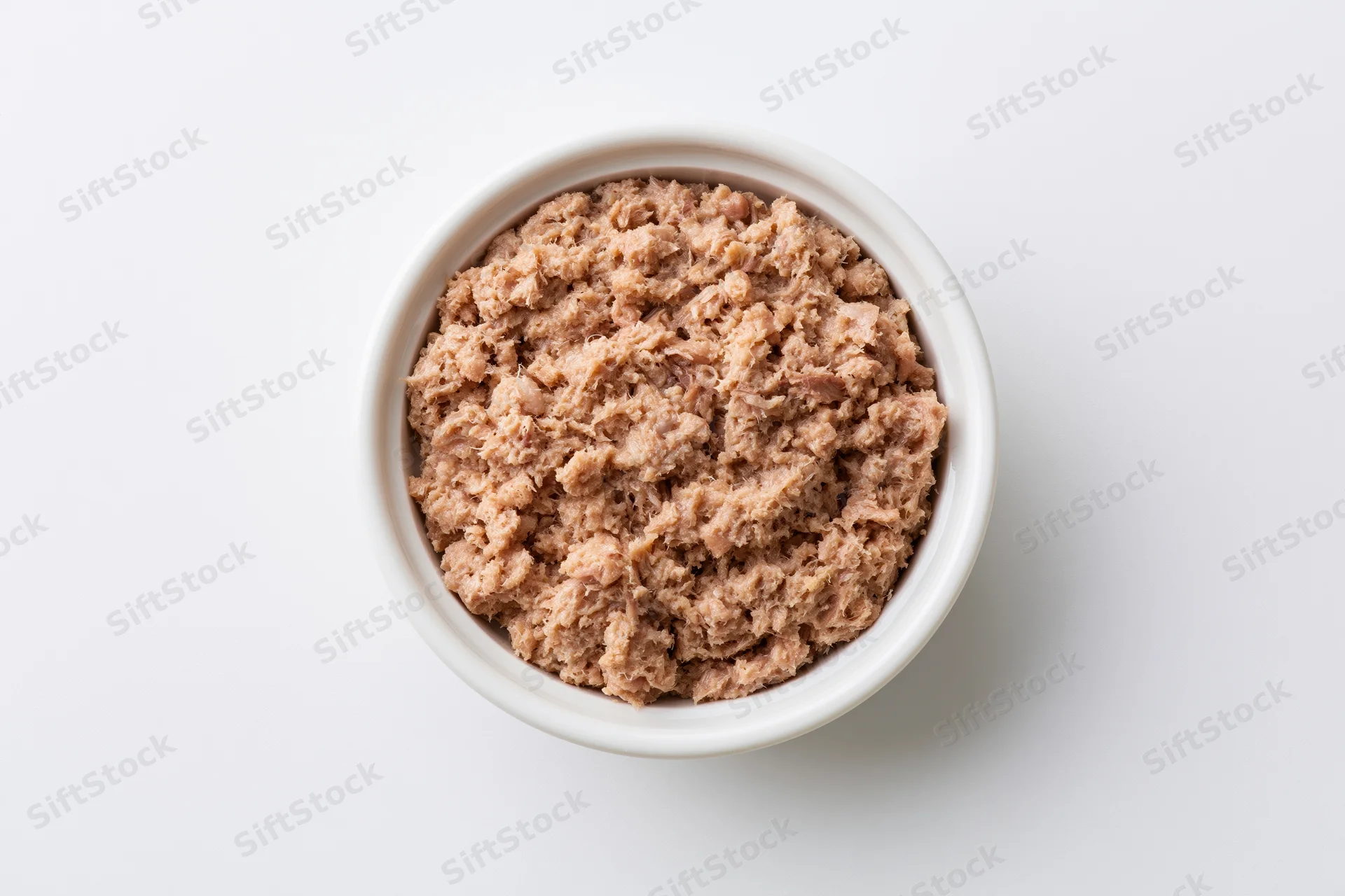 Chunky canned tuna in a white ceramic bowl viewed from above on a plain white surface