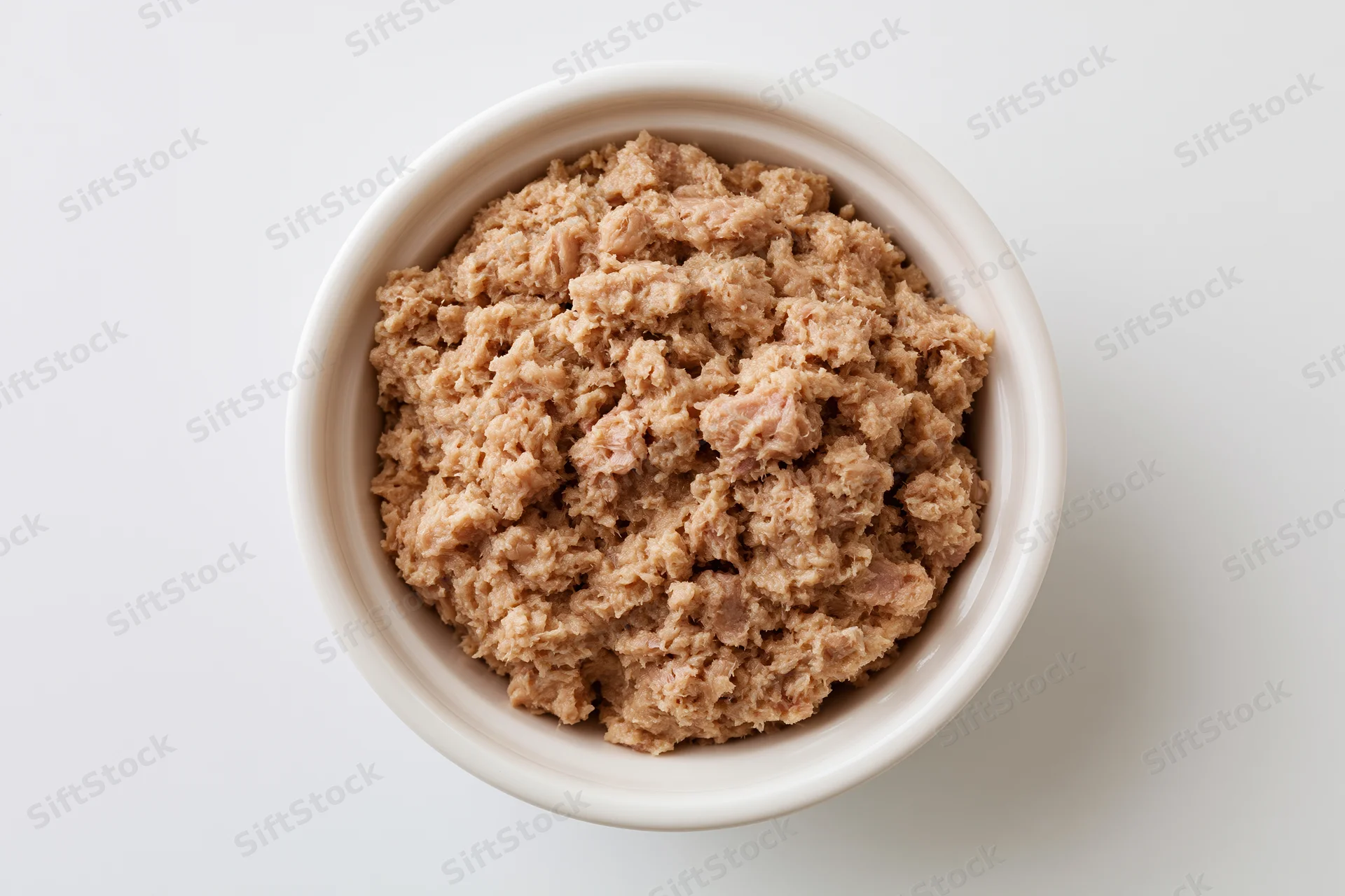 Chunky canned tuna in a white ceramic bowl viewed from above on a plain white surface