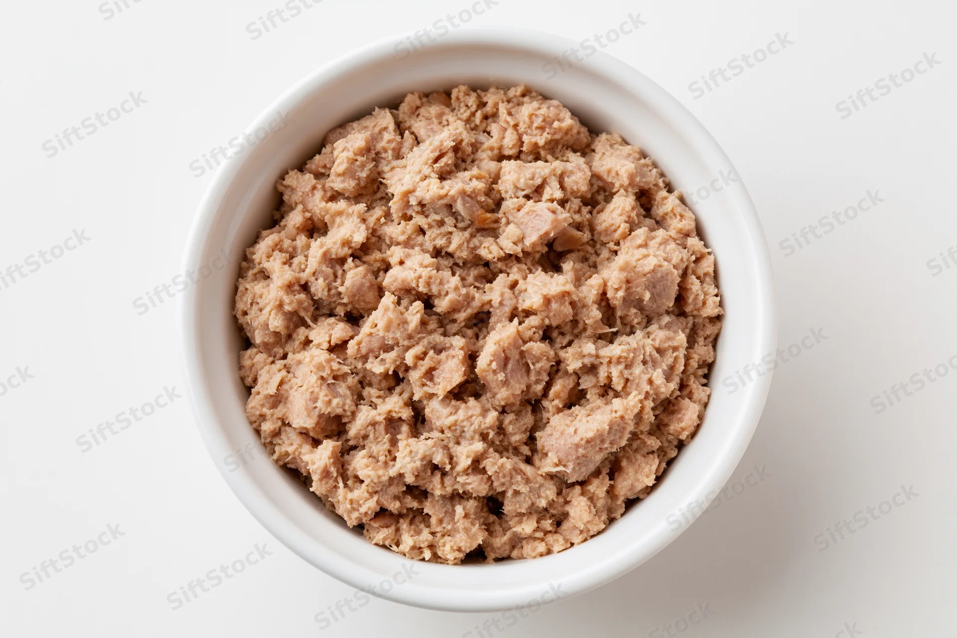 Chunky canned tuna in a white ceramic bowl viewed from above on a plain white surface