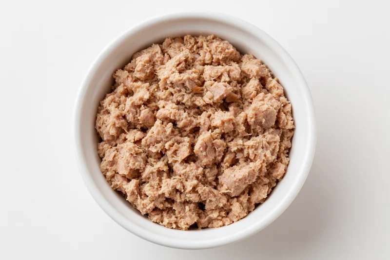 Chunky canned tuna in a white ceramic bowl viewed from above on a plain white surface