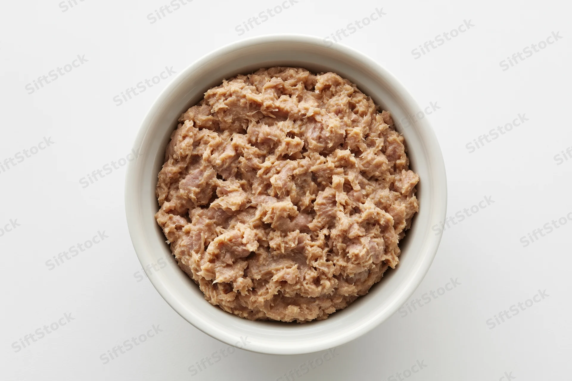 Chunky canned tuna in a white ceramic bowl viewed from above on a plain white surface