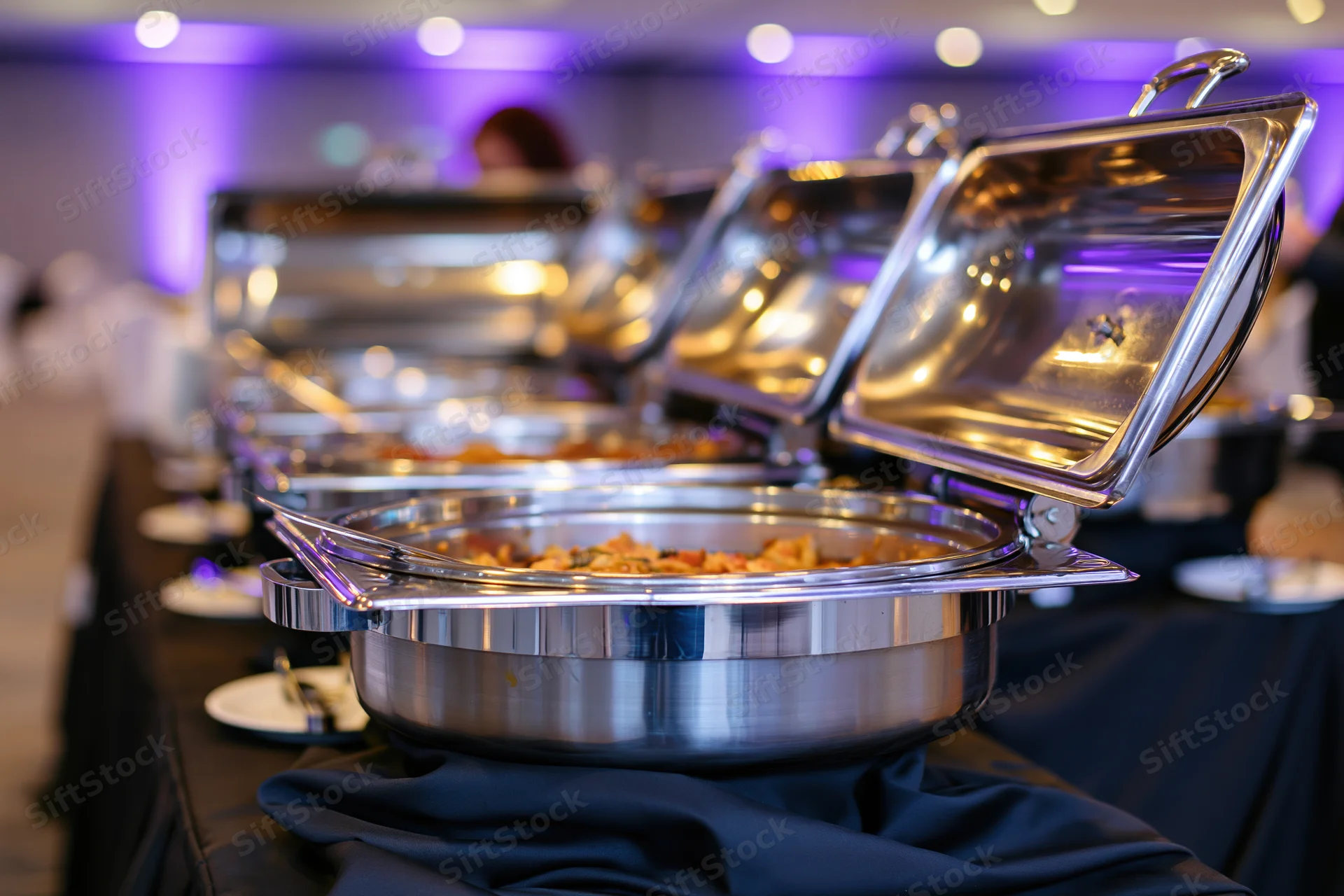 Row of stainless steel chafing dishes with open lids on a buffet table at an event
