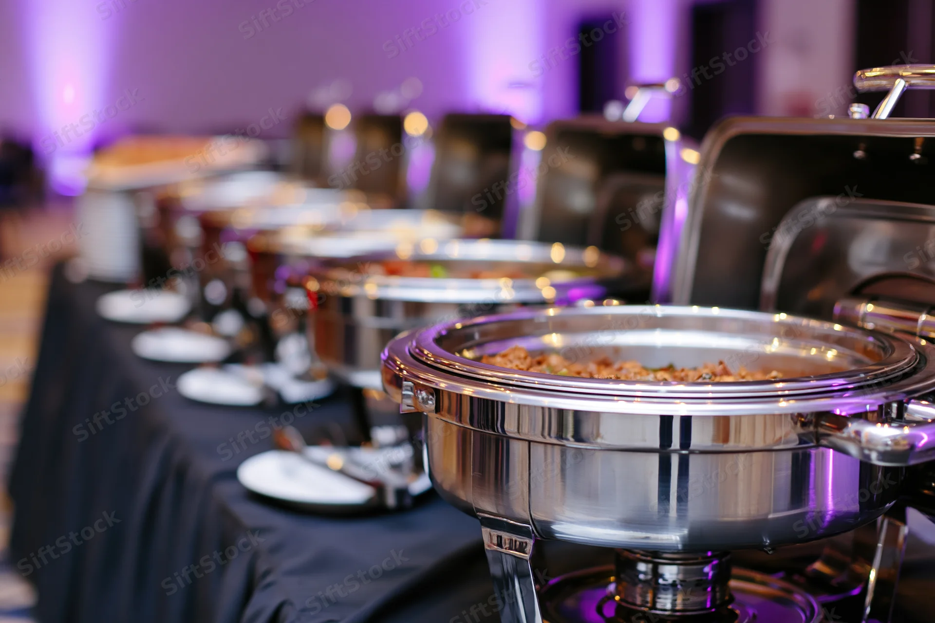 Row of stainless steel chafing dishes with open lids on a buffet table at an event