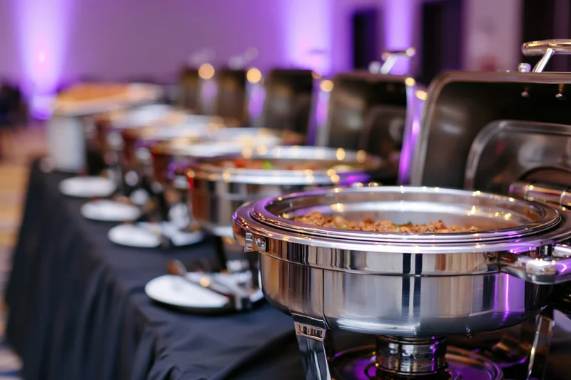 Row of stainless steel chafing dishes with open lids on a buffet table at an event