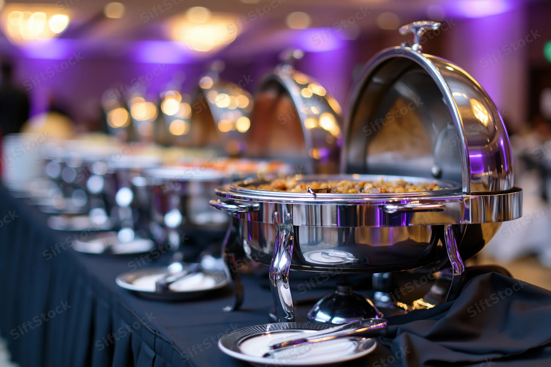 Row of stainless steel chafing dishes with open lids on a buffet table at an event