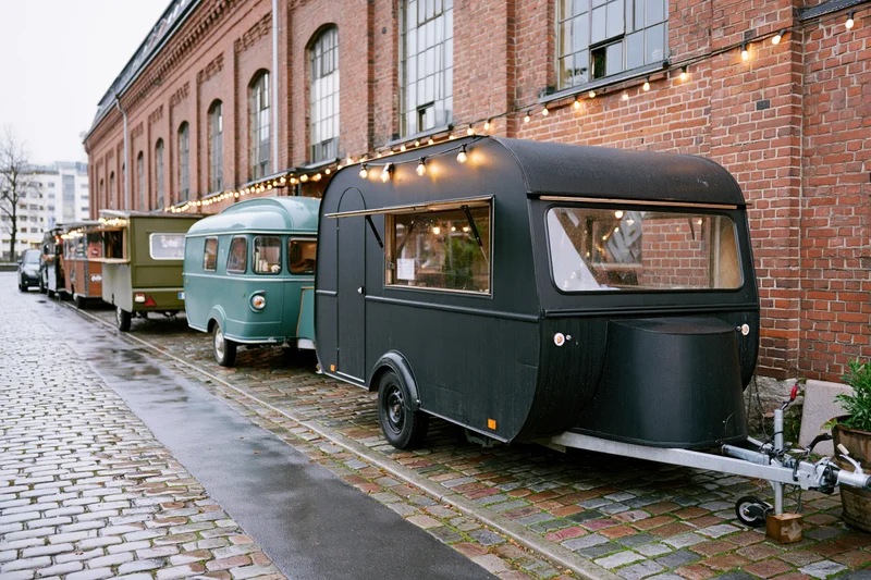 Vintage food trailers parked in a row along a wet cobblestone street beside a brick building with string lights