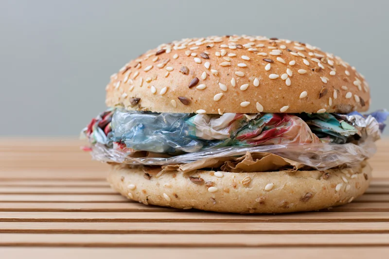 A burger with crumpled plastic waste inside, on a wooden slatted surface
