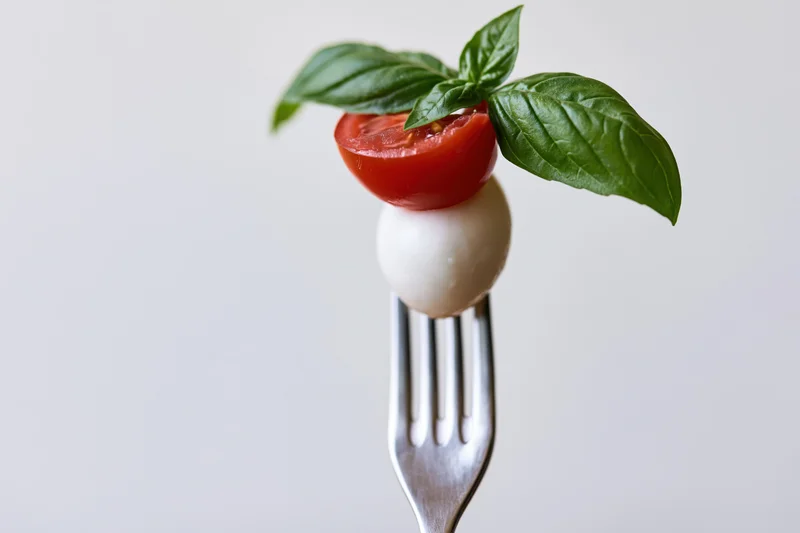 Caprese salad ingredients on a fork against a plain background