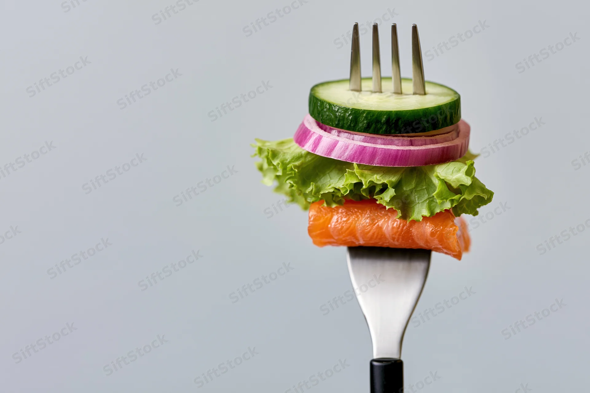 Fork holding stacked salmon, cucumber, lettuce and onion against white background