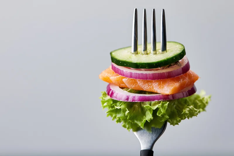 Fork holding stacked salmon, cucumber, red onion, and lettuce against a plain background