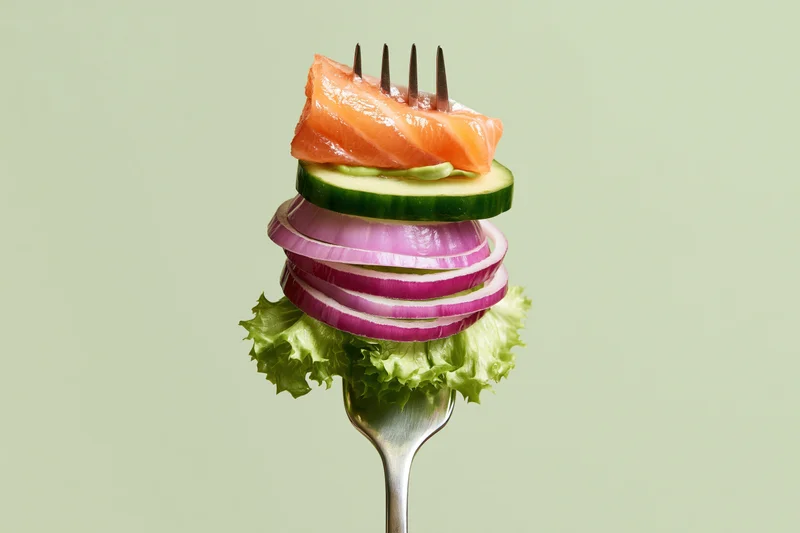 Fork stacked with salmon, cucumber, red onion and lettuce against light green background