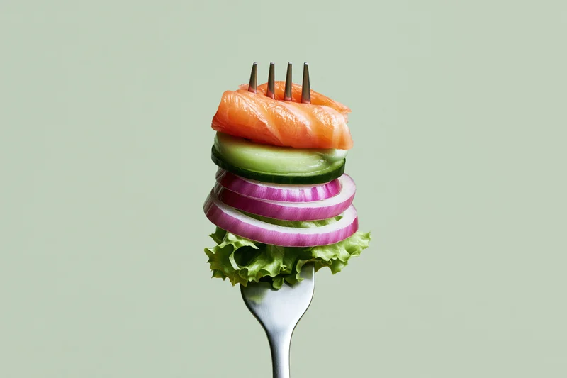 Fork holding stacked salmon, cucumber, red onion and lettuce against plain background