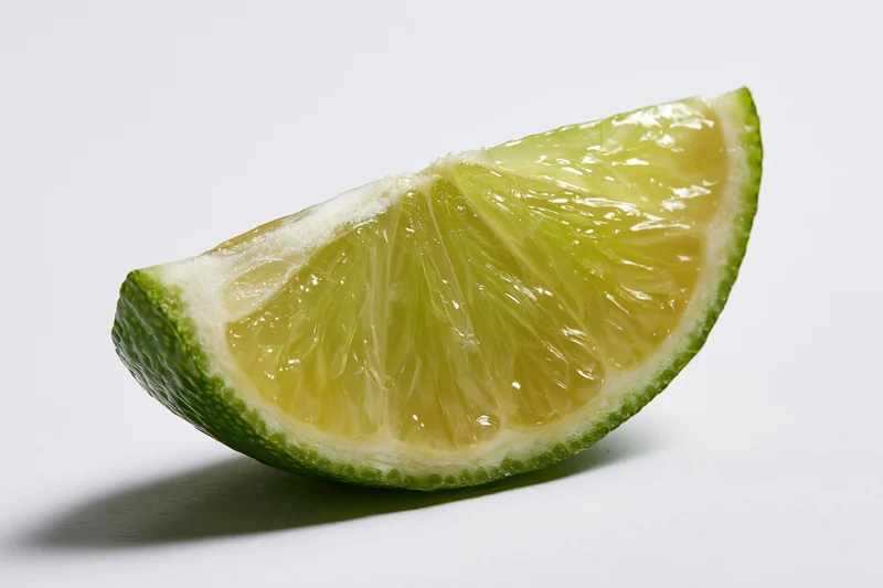 Lime wedge slice cut side facing forward on white surface