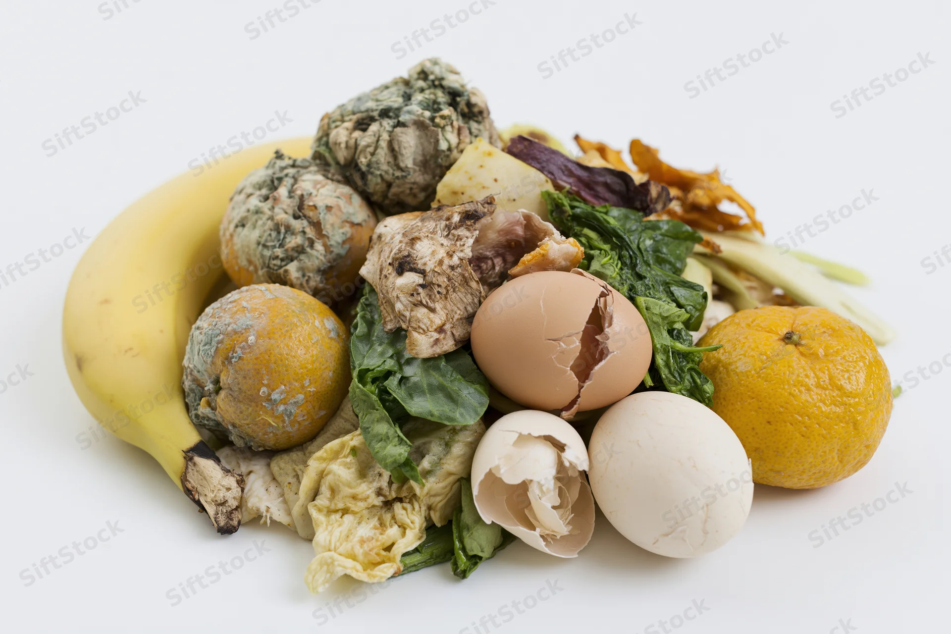 Pile of food waste and kitchen scraps including banana, oranges, eggshells, and leafy greens on white background