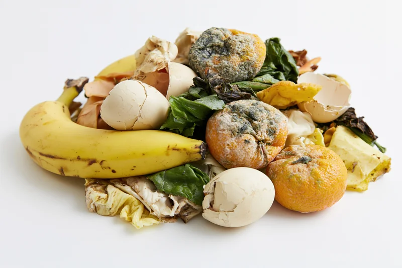 Pile of rotten fruit, vegetables, eggshells and peels on white background