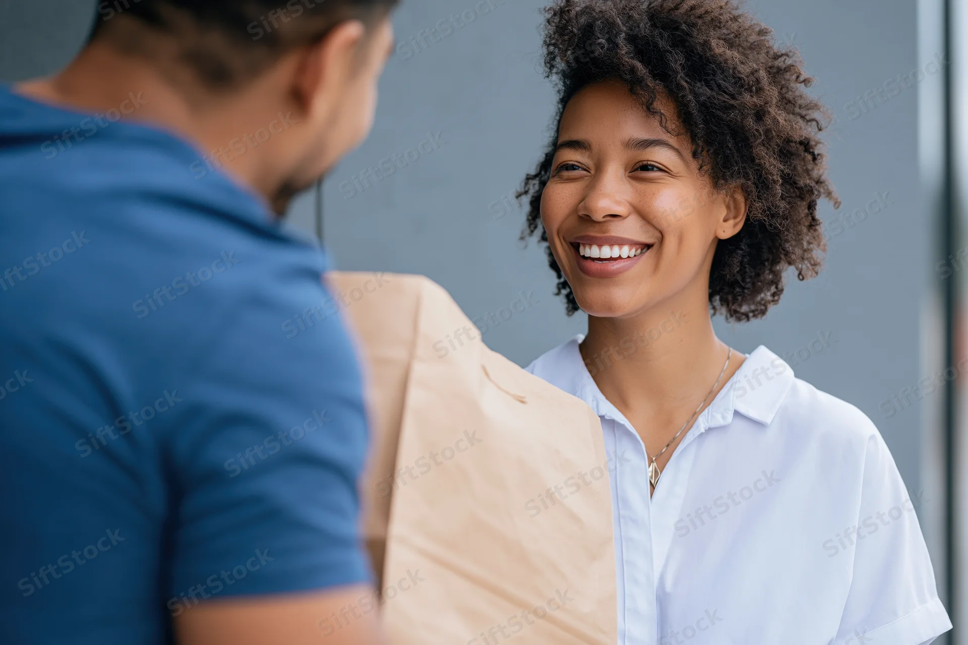 Smiling woman receiving a paper bag from a delivery person outdoors