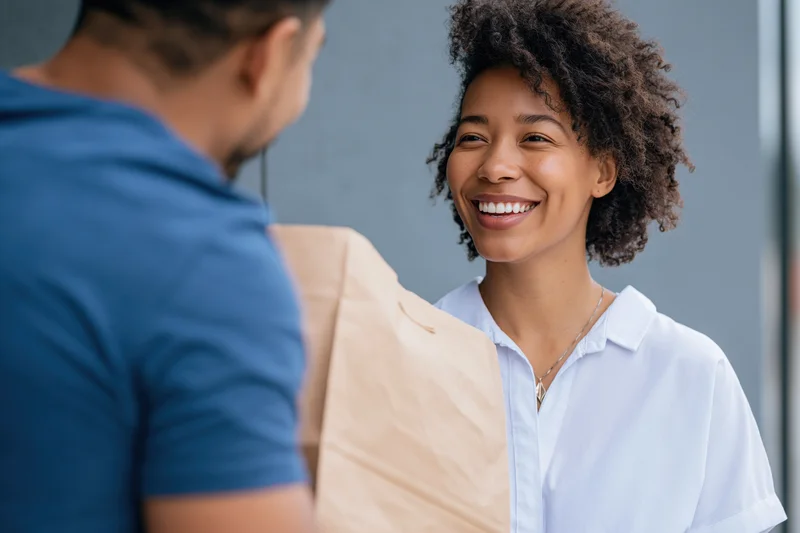 Smiling woman receiving a paper bag from a delivery person outdoors