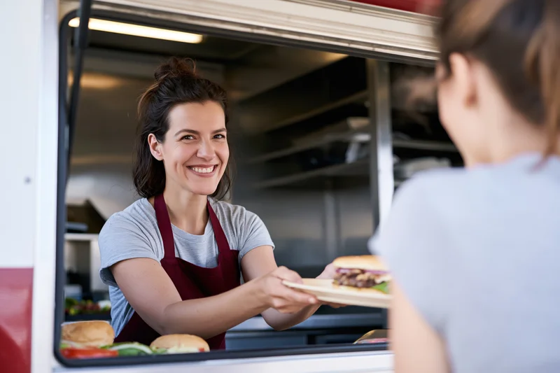 Woman in red apron serving burger to customer from food truck window