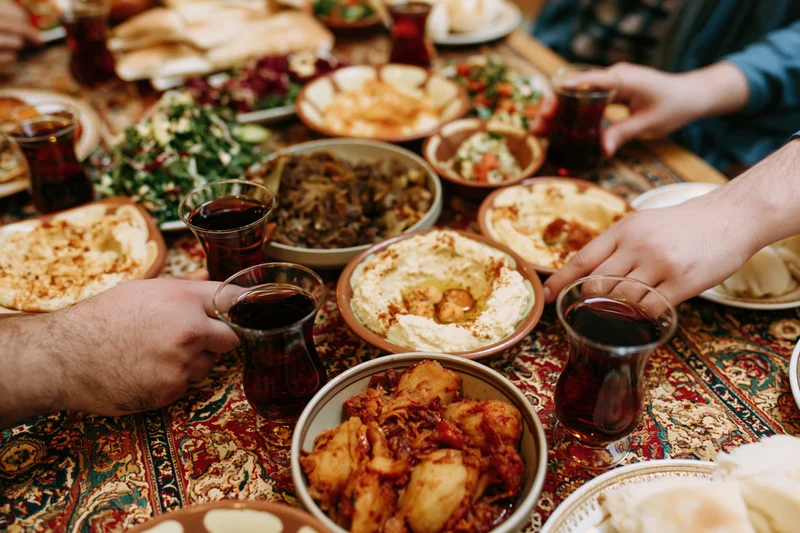 Hands reaching for mezze dishes on a patterned tablecloth during a shared meal