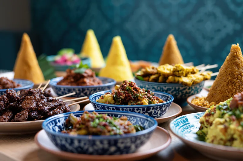 Traditional indonesian dishes arranged on a table with blue patterned bowls and yellow rice cones
