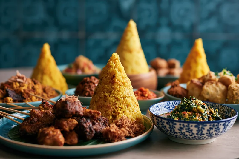Traditional indonesian dishes arranged on a table with cone-shaped rice and satay skewers