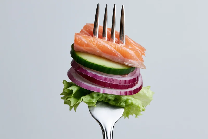 Fork holding stacked salmon, cucumber, red onion, and lettuce against white background