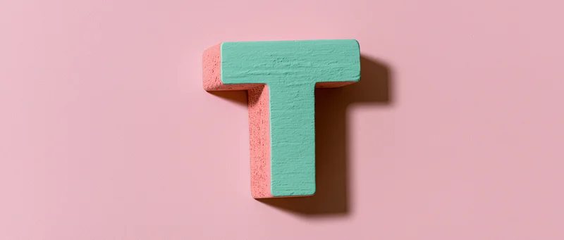 Wooden letter t mounted flat against a pink wall