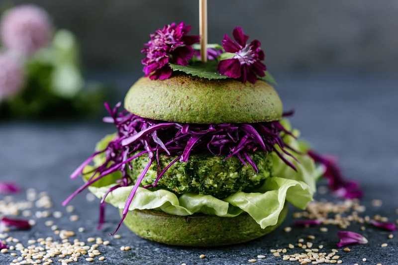 Vegan avocado bun burger with green herb patty and purple cabbage on dark stone surface