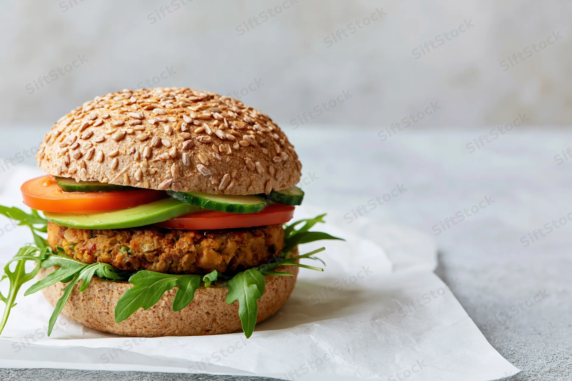 Vegan burger with chickpea patty and fresh vegetables on a seeded bun, placed on parchment paper on a light surface
