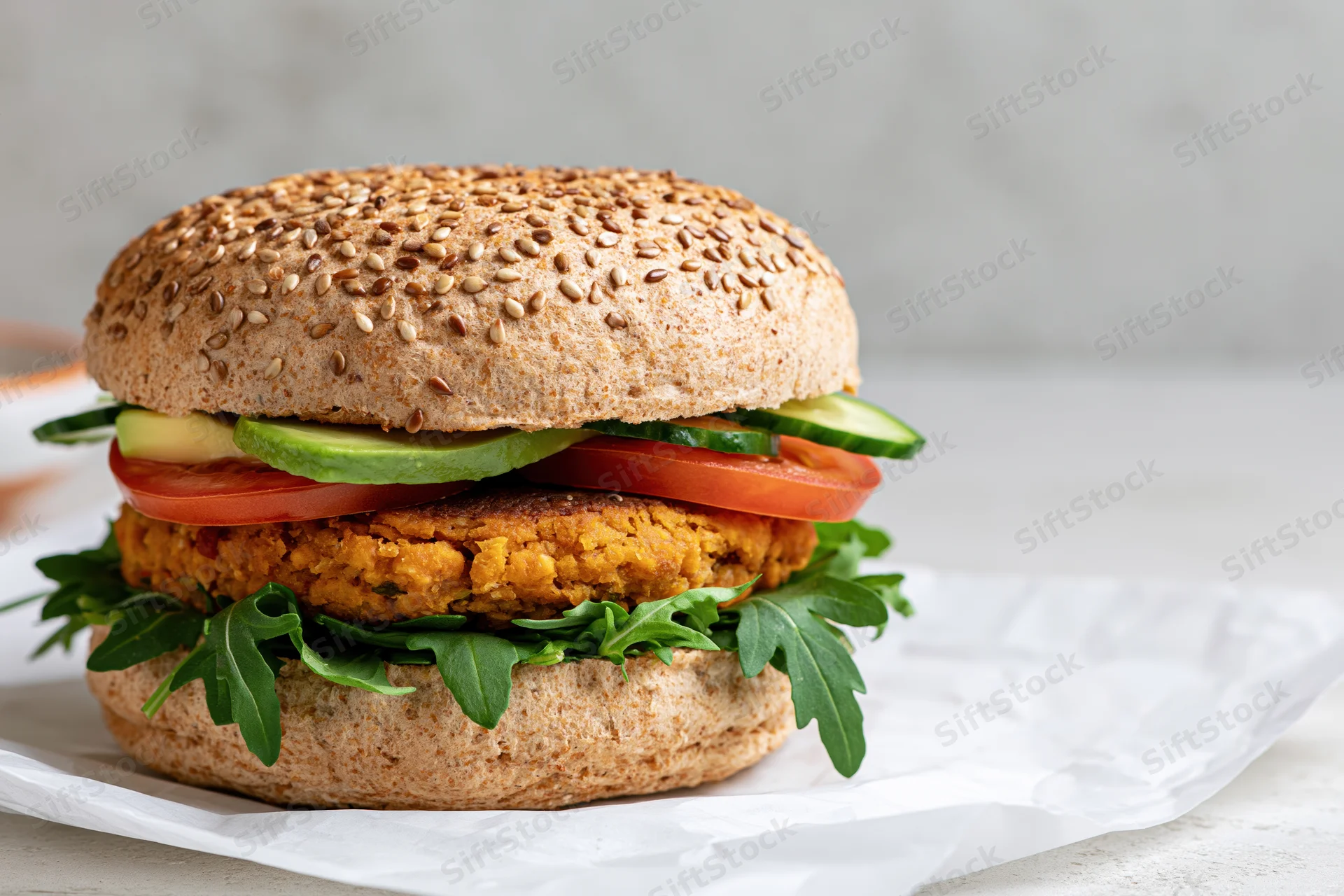 Vegan burger with chickpea patty and fresh vegetables on a seeded bun, served on crumpled paper