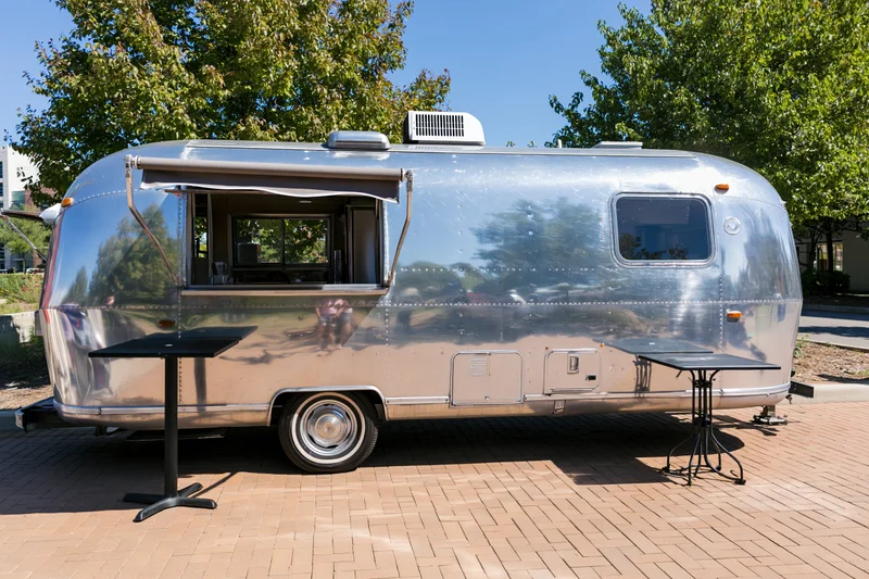 Vintage polished aluminum airstream trailer with open window and tables on brick patio outdoors
