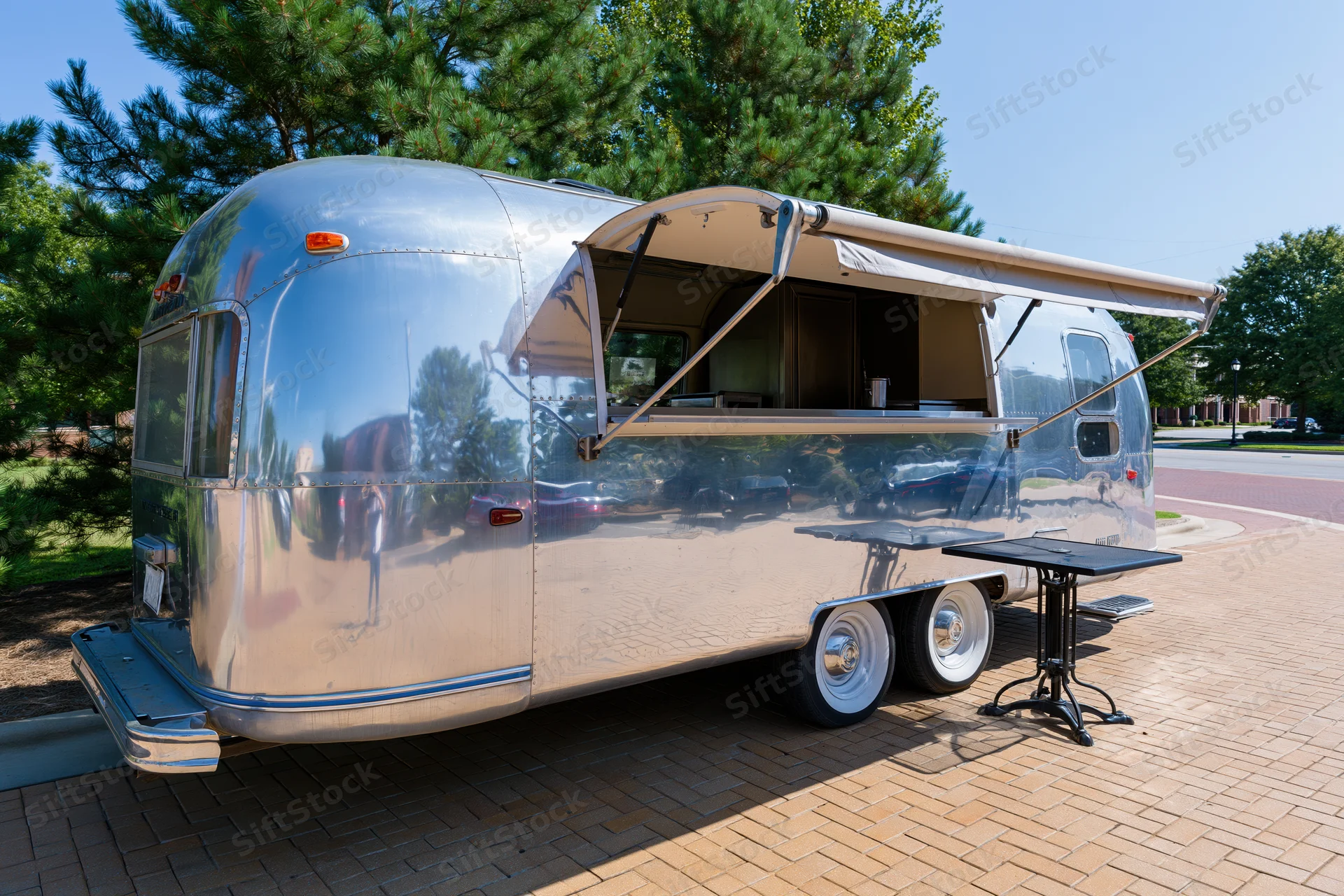 Vintage aluminum airstream trailer converted into a food truck with awning extended on brick pavement outdoors