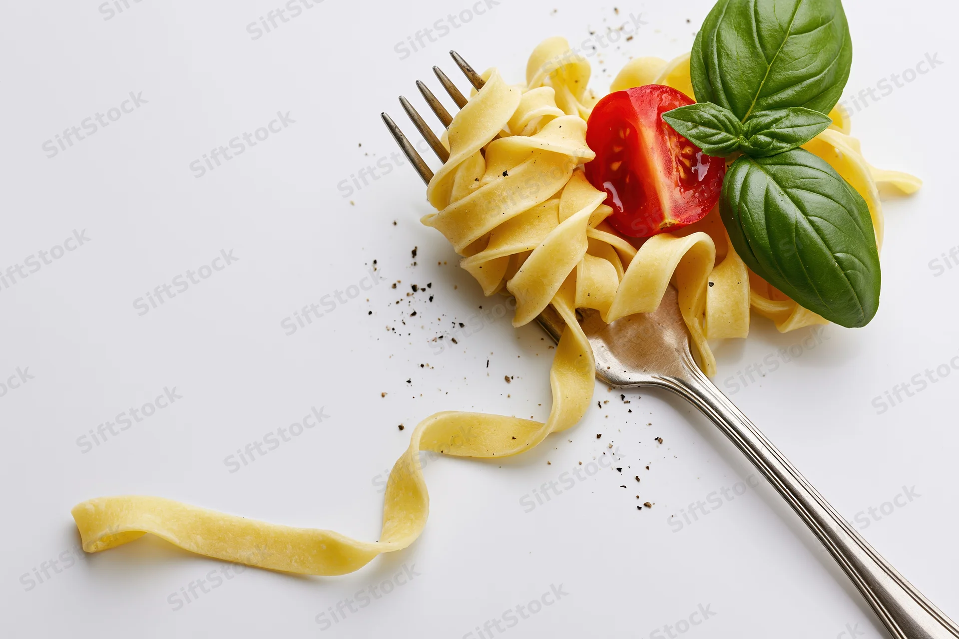 Vintage silver fork holding twisted tagliatelle pasta with basil and tomato on white surface