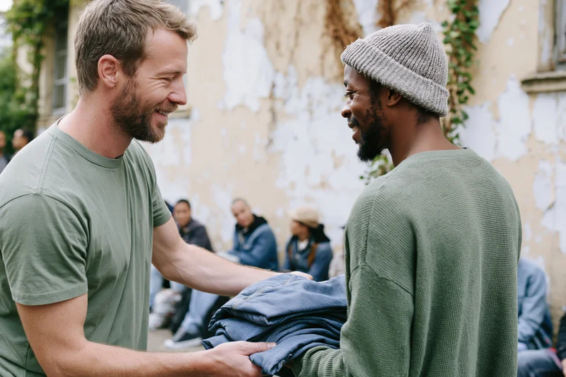 Volunteer handing folded denim clothing to a man on a city street