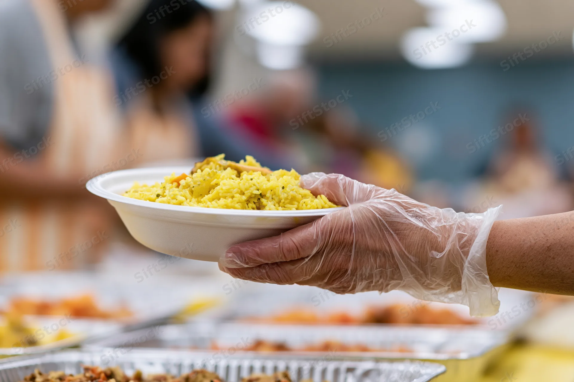 Volunteer's gloved hand holding a white bowl of yellow rice at a food distribution event