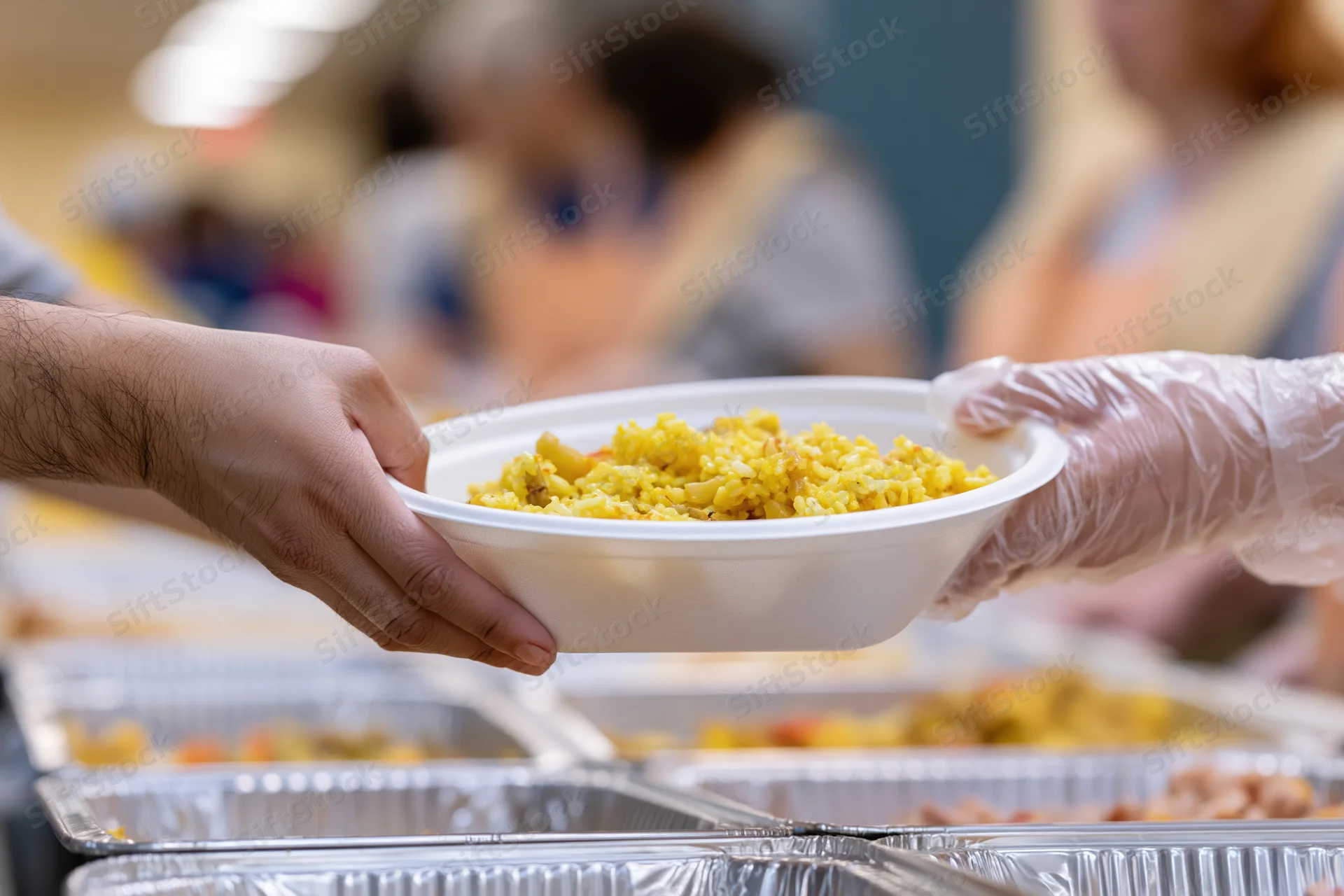 Volunteer handing a white bowl of yellow food to a recipient at a charity meal service