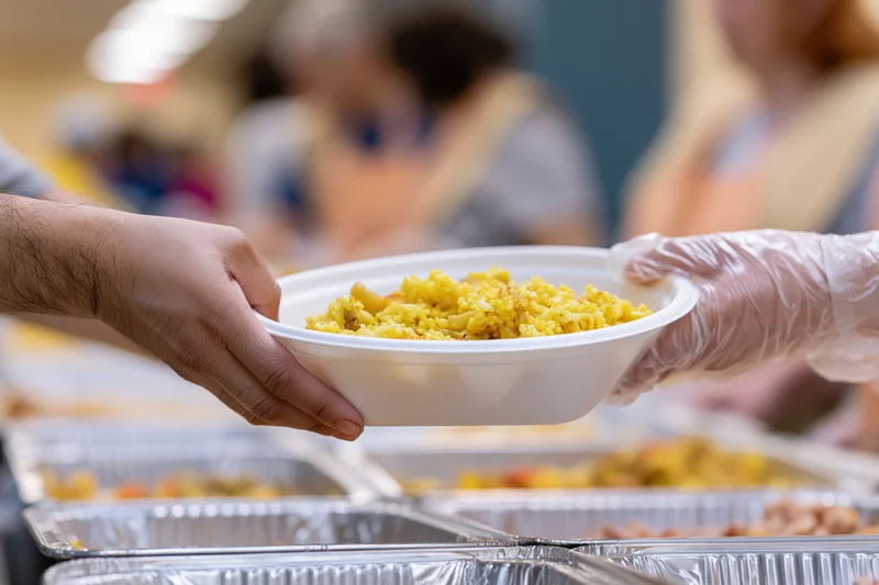 Volunteer handing a white bowl of yellow food to a recipient at a charity meal service