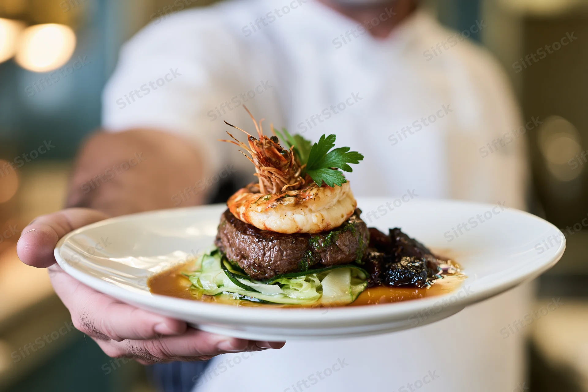 Chef holding a plated steak topped with shrimp and garnish in a restaurant