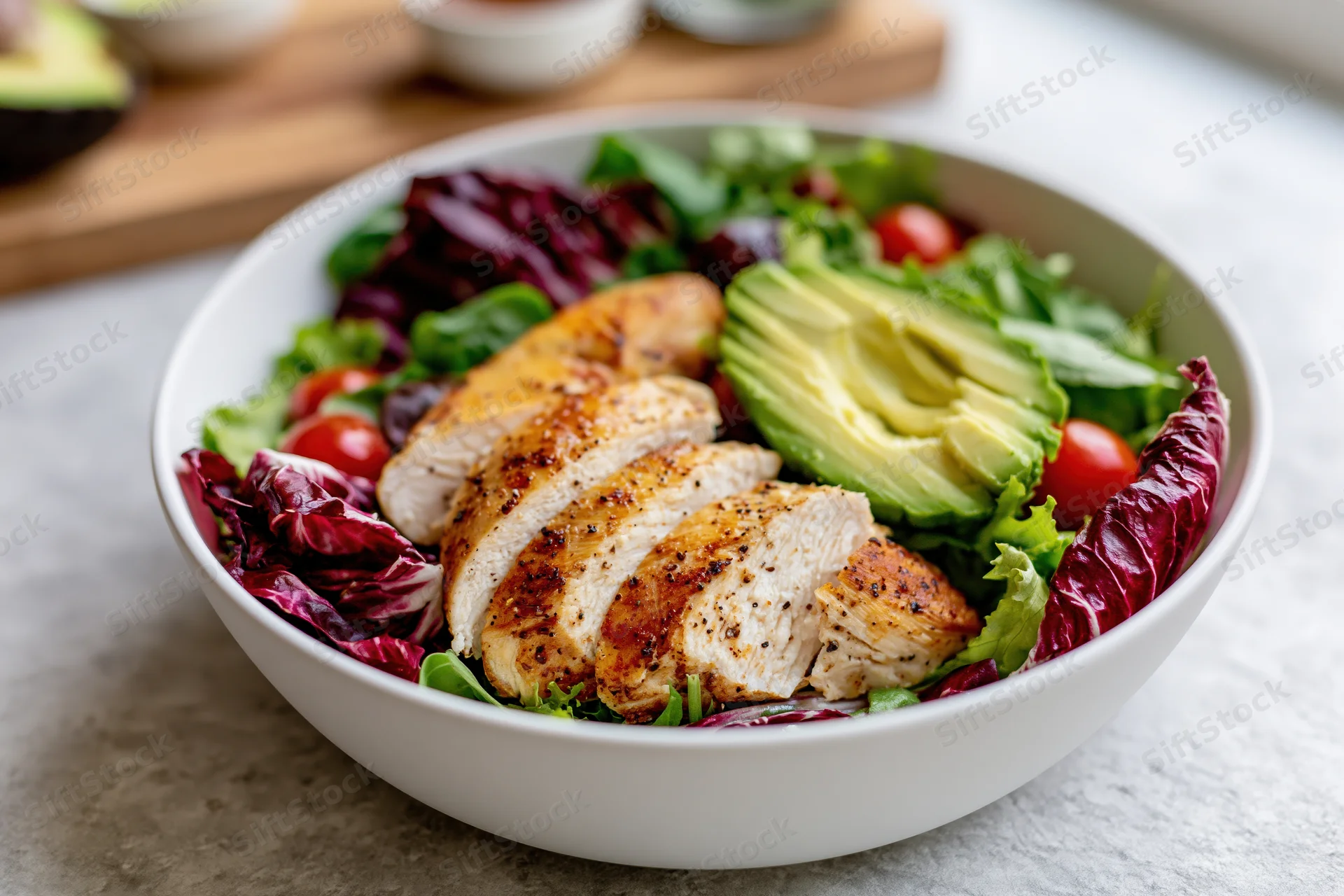 Grilled chicken salad with avocado and mixed greens in a white bowl on a kitchen countertop