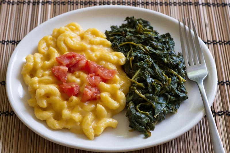 Creamy macaroni and cheese with spinach and tomato on a white plate with fork on bamboo mat