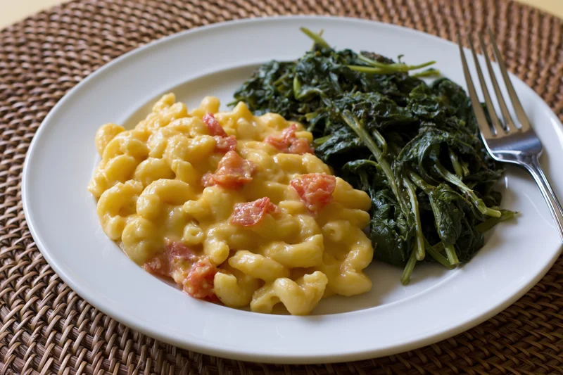 Creamy macaroni and cheese with spinach on a white plate on a woven placemat