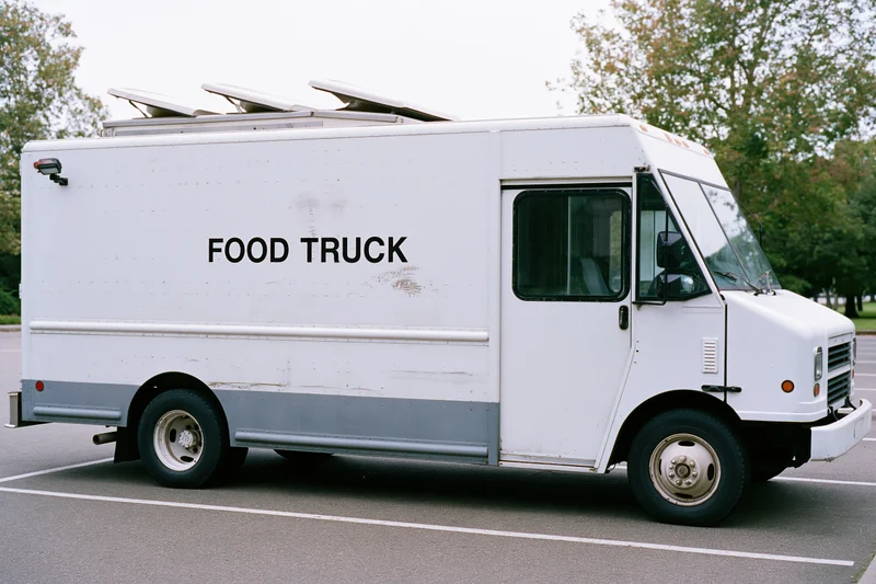 White food truck parked in lot with driver door open and roof vents visible