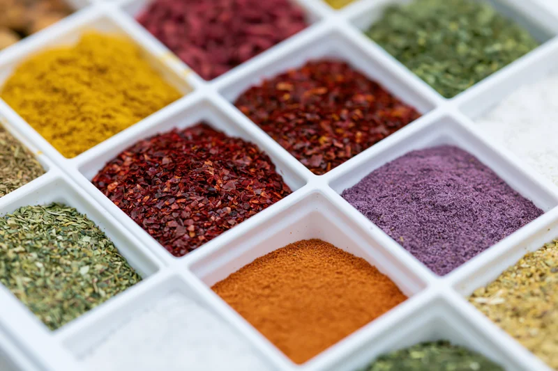 White plastic tray with compartments filled with various colorful spices arranged in a grid pattern