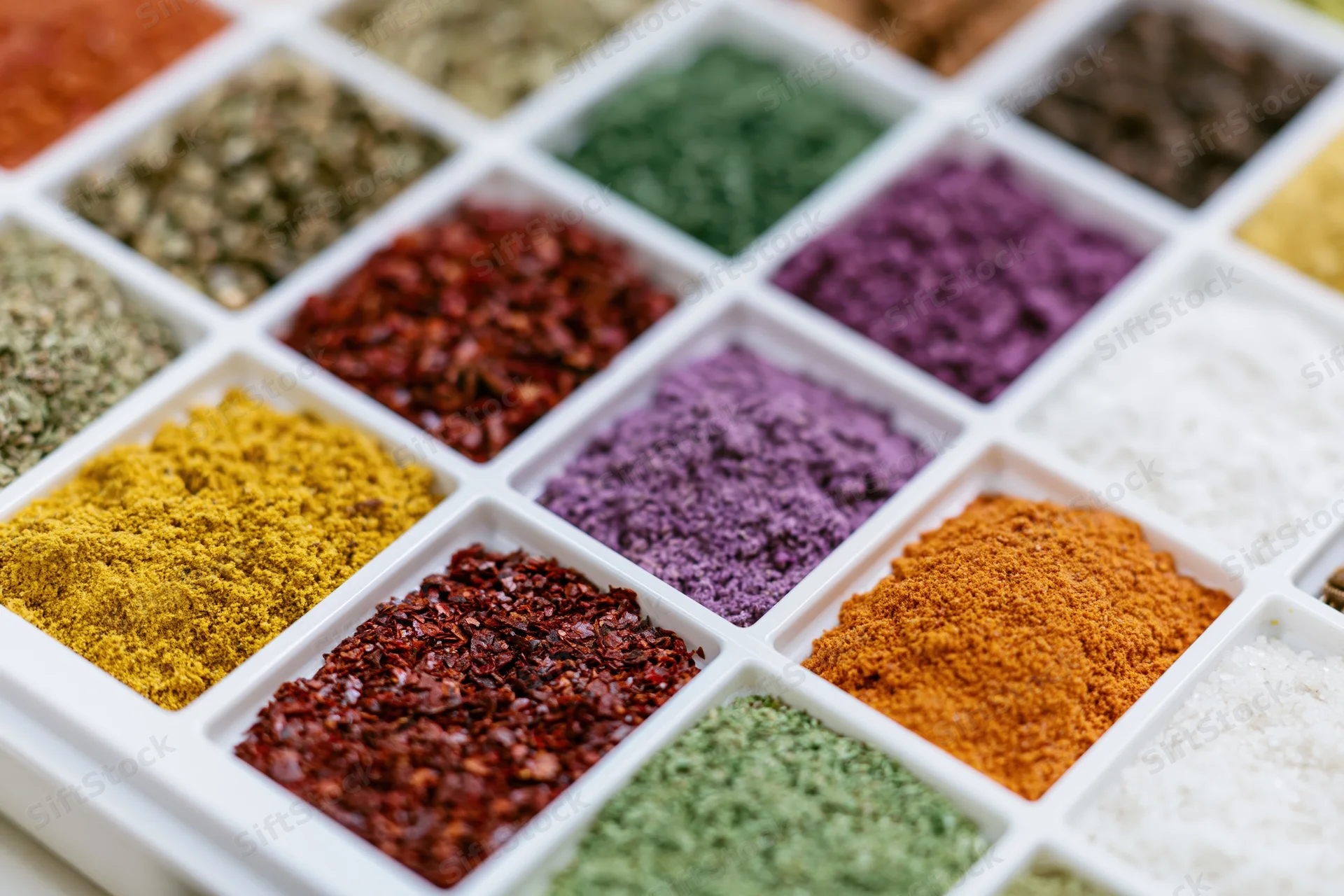 Colorful spices arranged in a white plastic tray grid for culinary display
