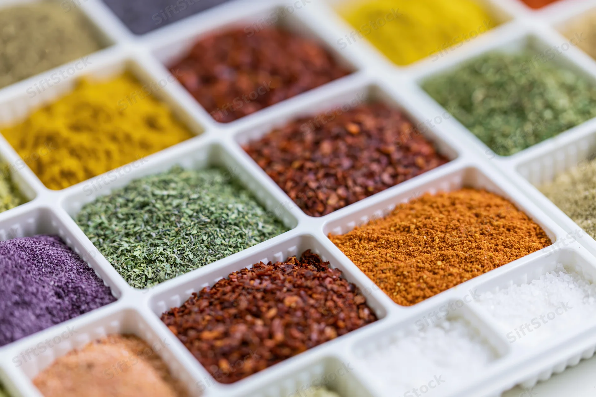 White plastic tray with multiple compartments filled with colorful spices arranged in a grid pattern